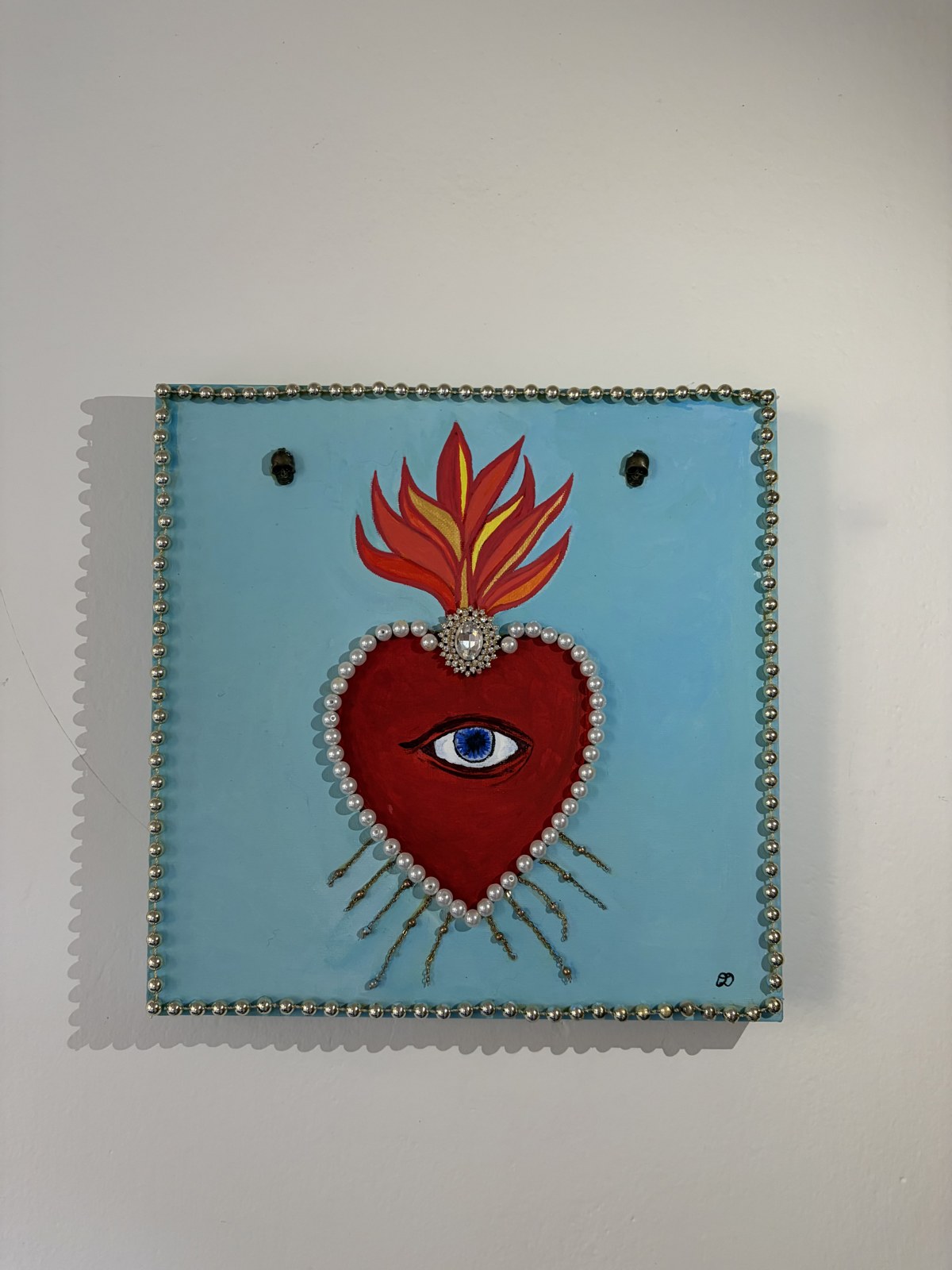Sacred Heart painting — a red flaming heart with a blue eye, framed in pearls on a light blue canvas